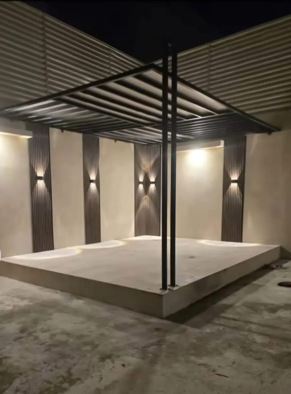 صالة واسعة بسقف جبس هندسي مضاء وجدار تلفزيون خشبي وقاطع خشبي عند المدخل